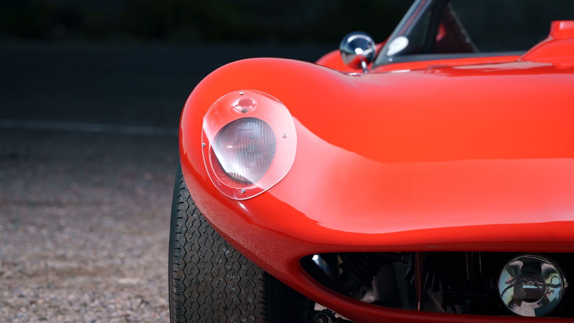 The headlight of a bright red 1960s sports car