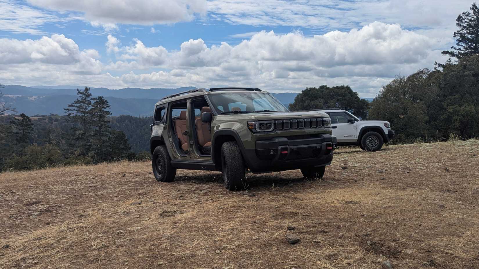 A red 2026 Jeep Recon EV driving through a wooded forest trail with its doors removed